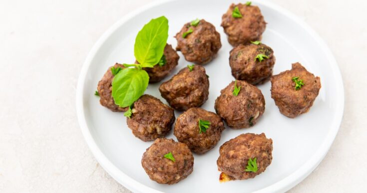 Oven cooked keto meatballs garnished with parsley and basil on a white plate