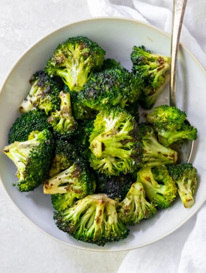 broccoli in a white bowl with a fork and a white napkin