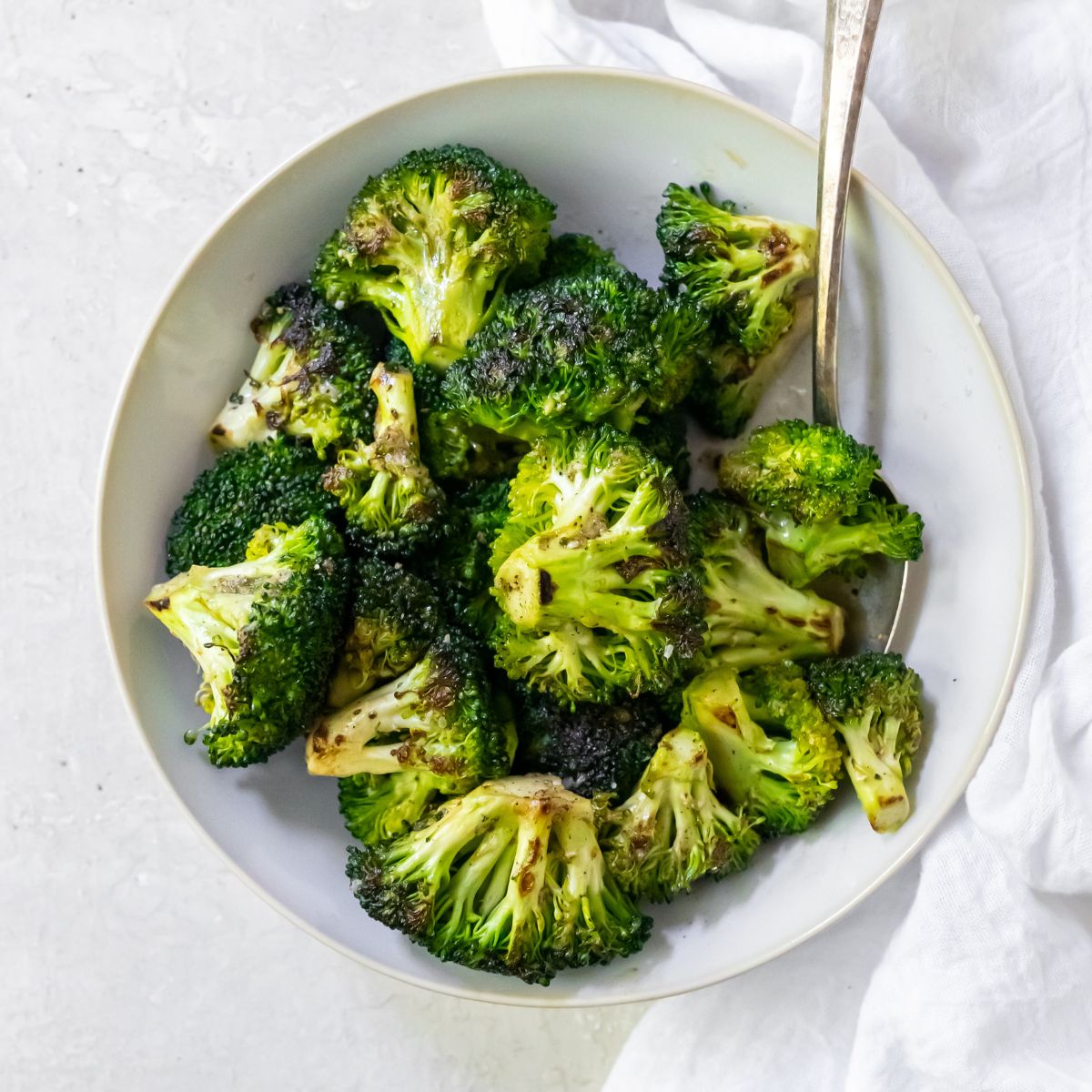 broccoli in a white bowl with a fork and a white napkin