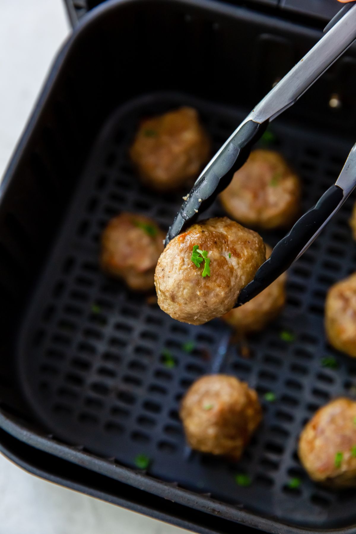 Cooked frozen meatball in the air fryer basket with a meatball in tongs