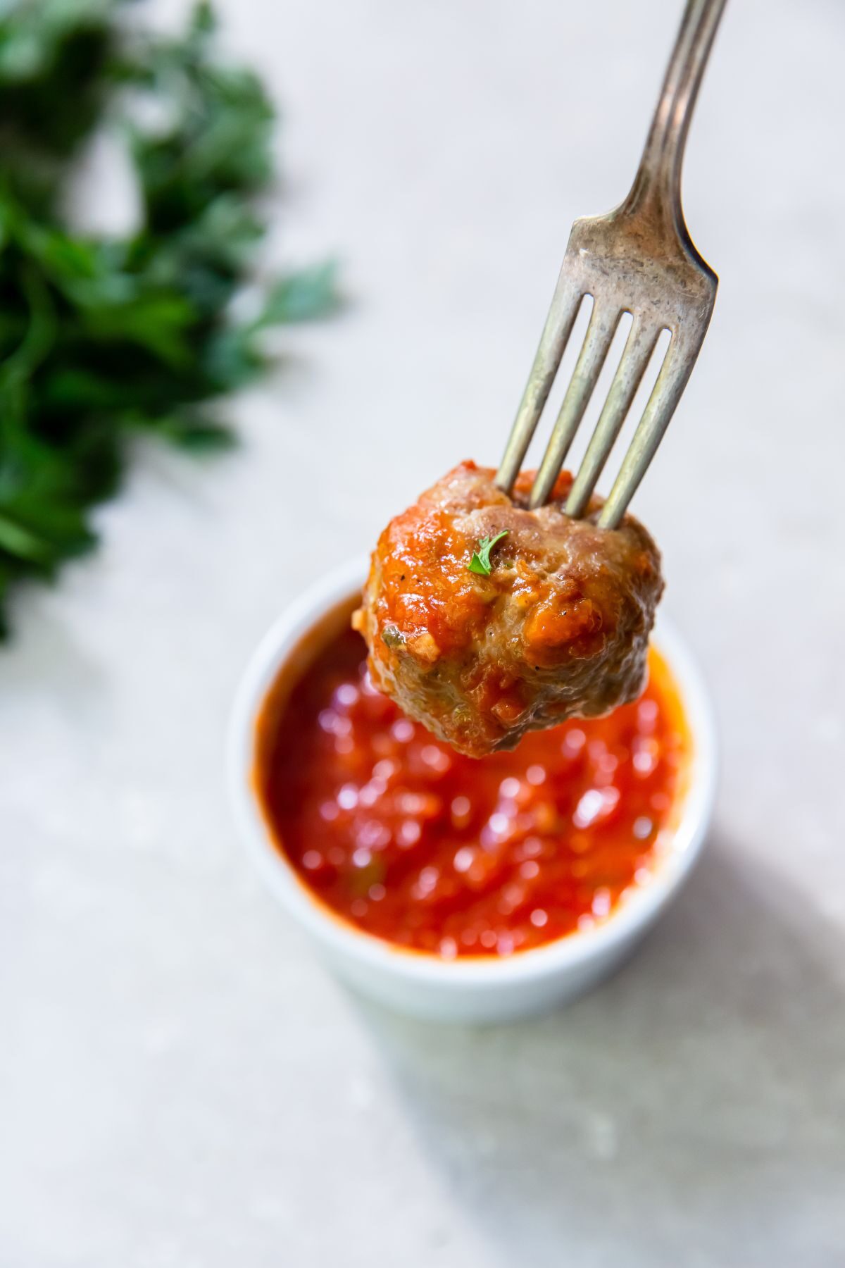 cooked frozen meatball on a fork with a small bowl of marinara