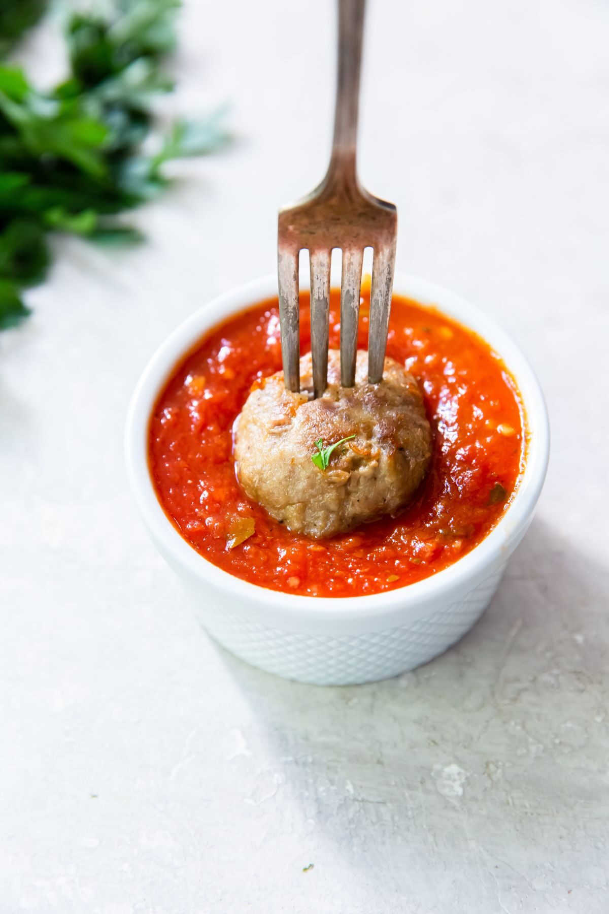 cooked frozen meatball on a fork with a small bowl of marinara