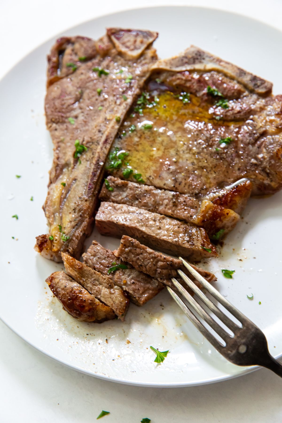 Air Fryer T-bone steak on a white plate butter and parsley on top. fork on plate