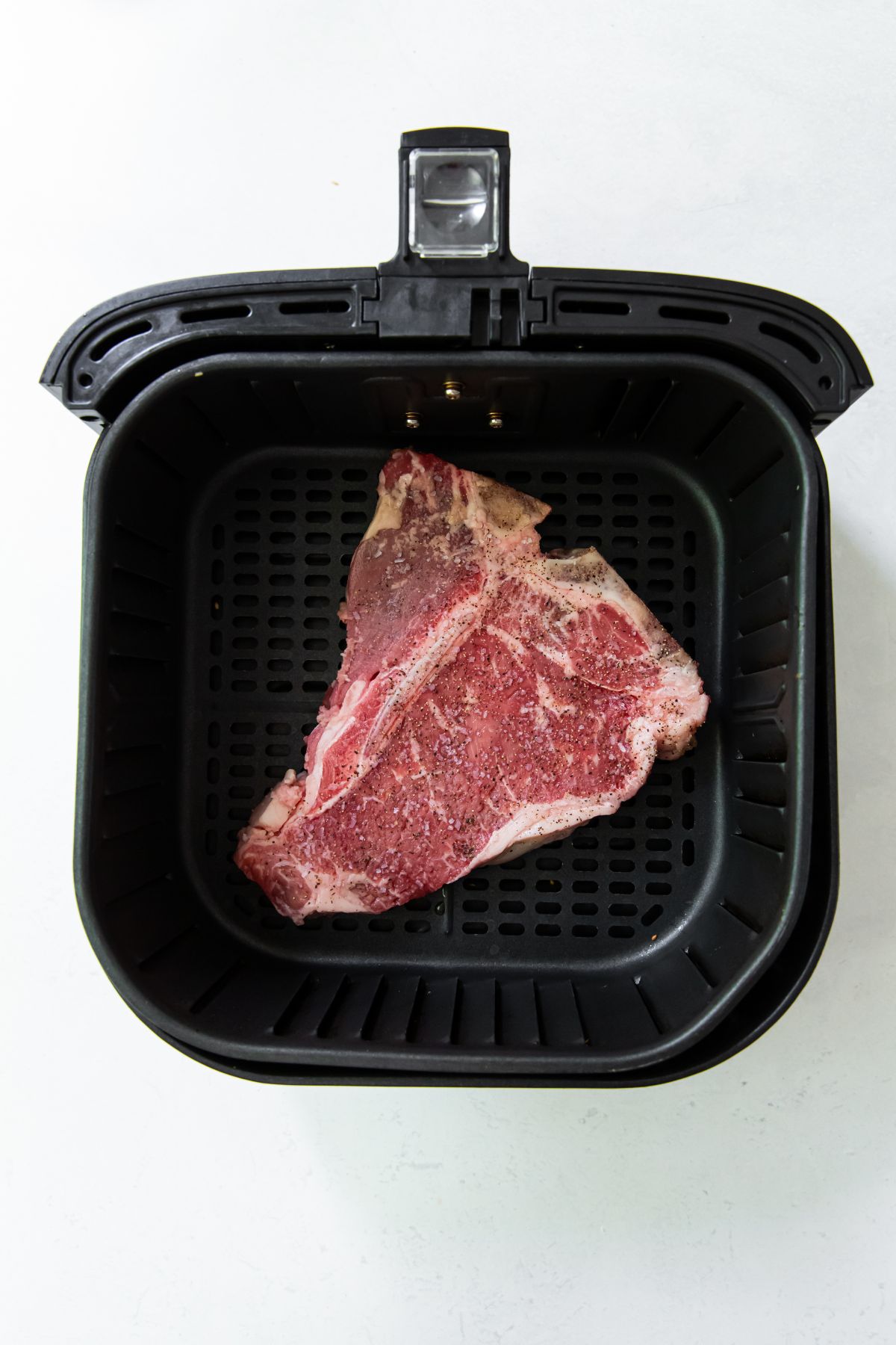 Black air fryer with raw steak inside