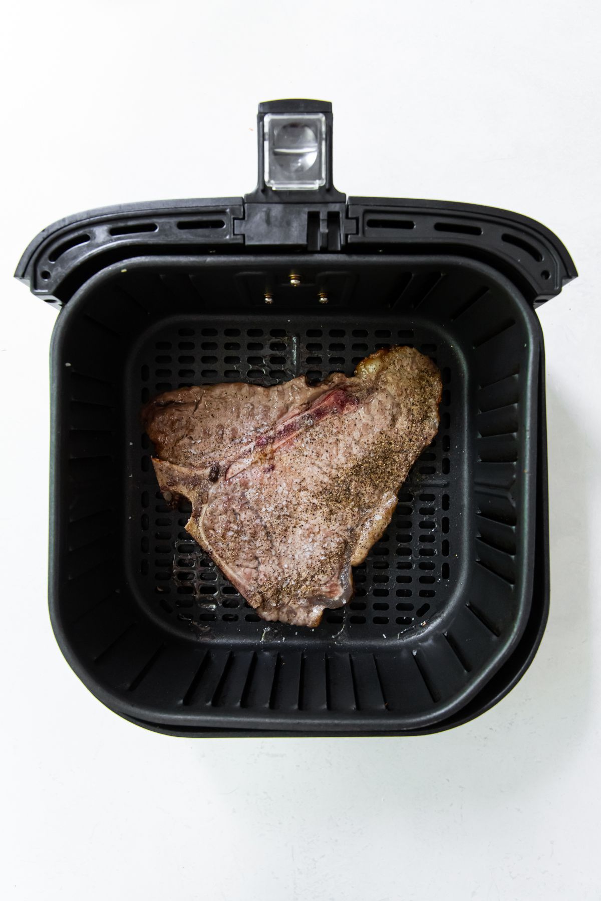 black air fryer with cooked steak inside