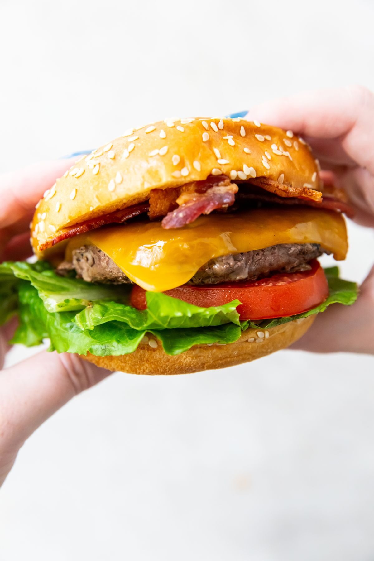 a blackstone burger being held in 2 hands topped with bacon, cheese, tomato and lettuce
