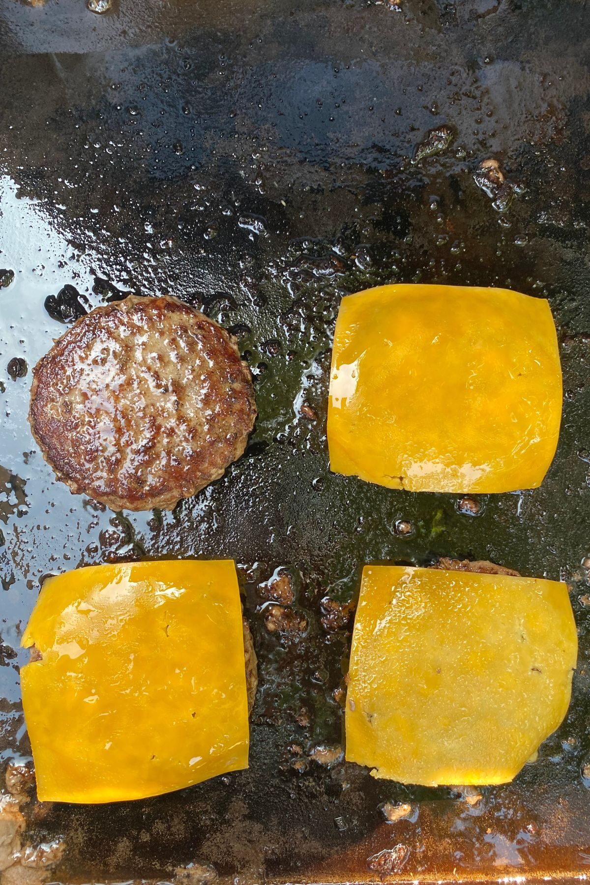 cooked hamburgers on a Blackstone with cheese on three of them.