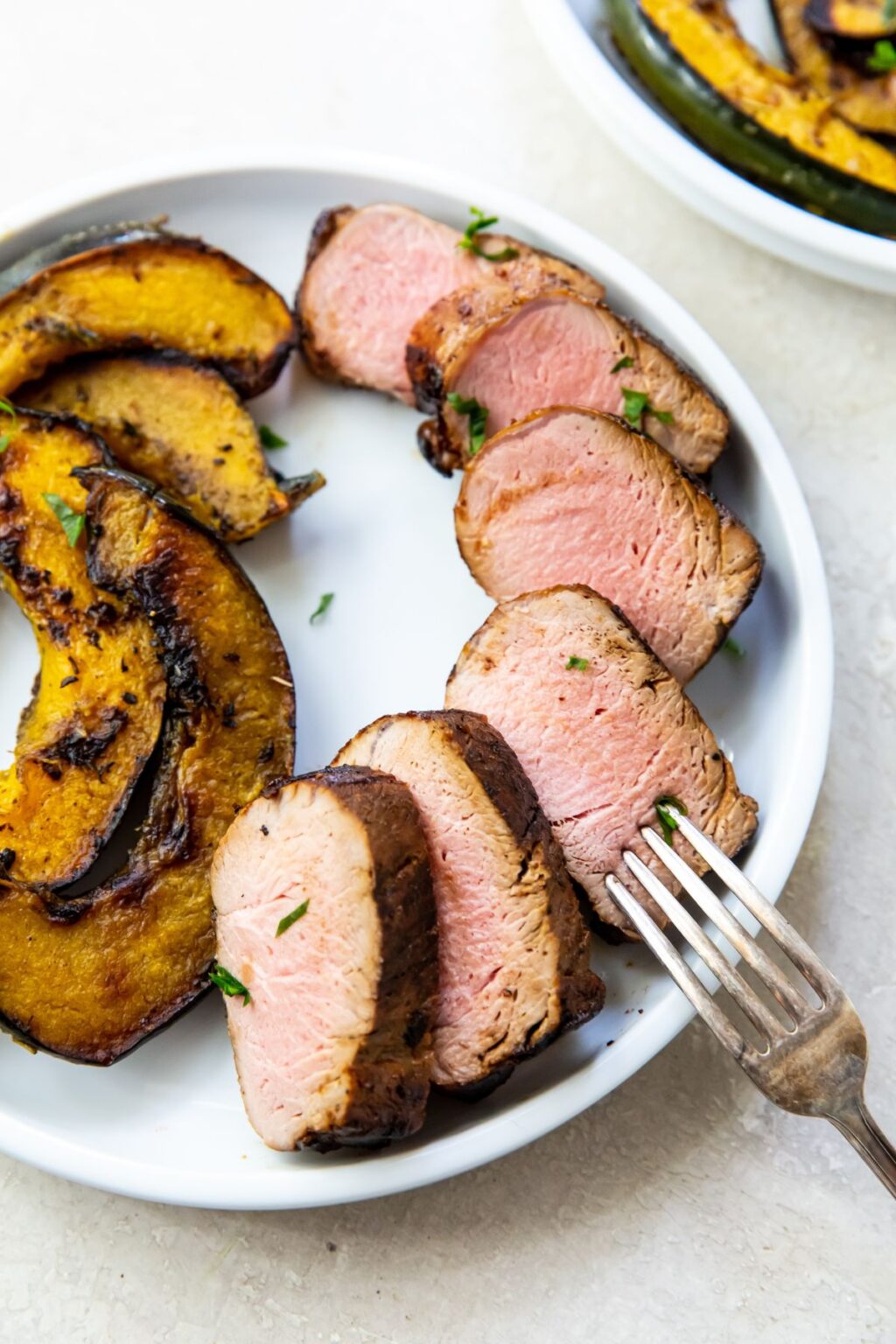 Blackstone Pork Tenderloin with squash and parsley on a white plate with a fork