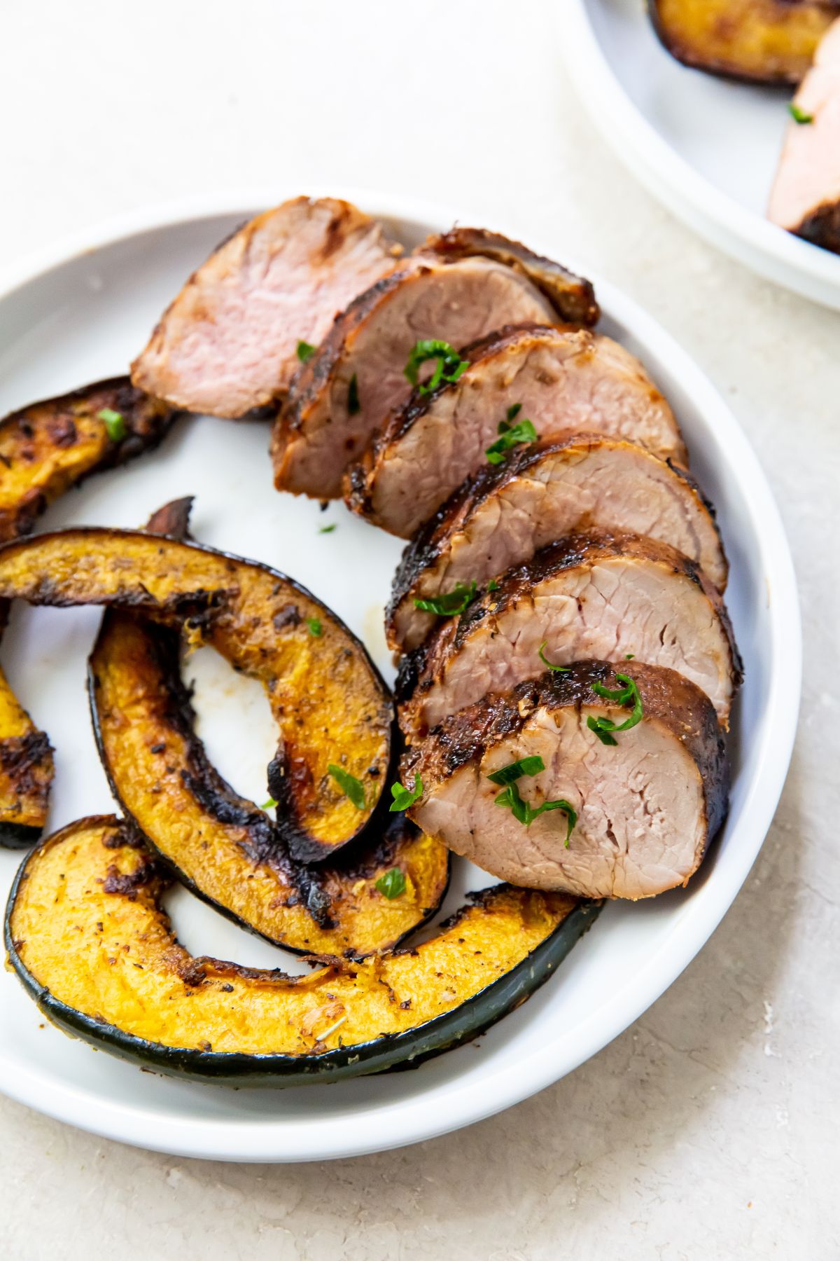 white plate with pork tenderloin and acorn squash next to it