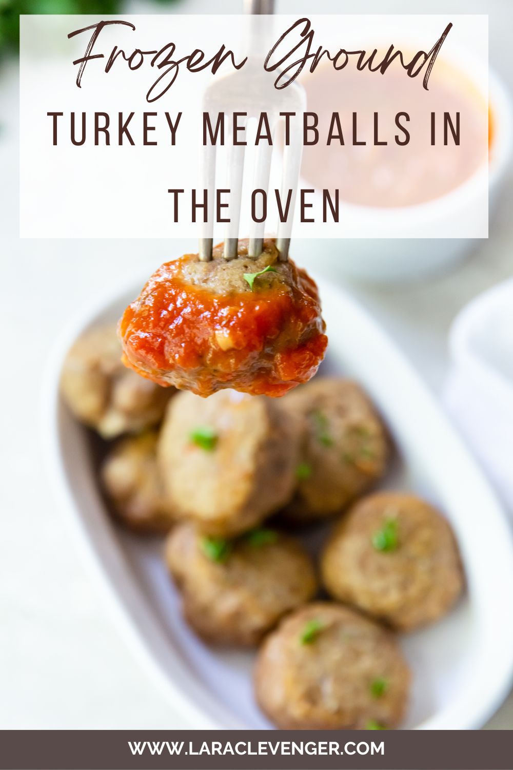 pin of cooked oven turkey meatballs on a white casserole dish with a meatball with marinara on a fork