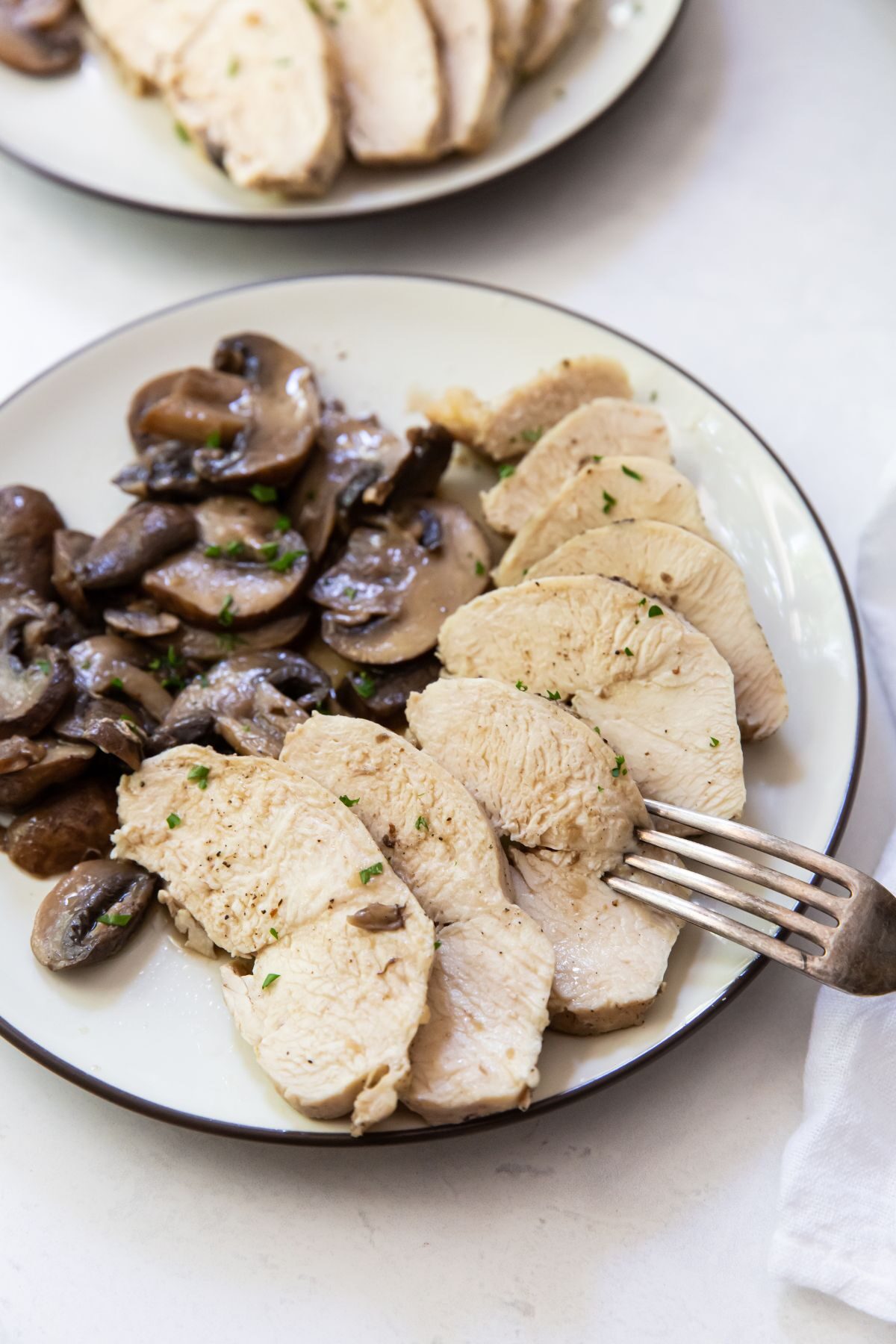 white plate with chicken and mushrooms fork on plate white napkin on the side