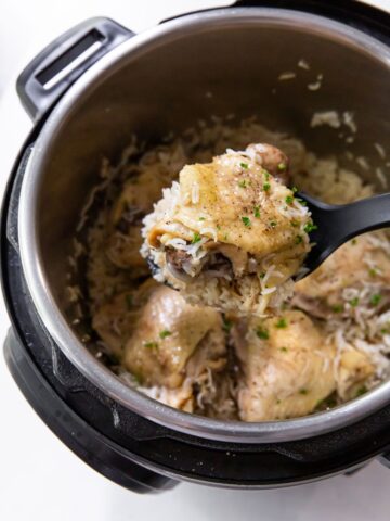 instant pot chicken thighs with rice with a spoon lifting a chicken thigh out of the instant pot