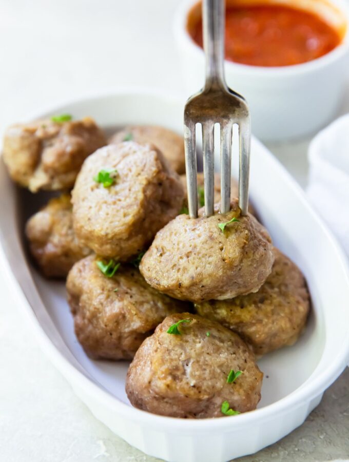 cooked oven turkey meatballs on a white casserole dish with a meatball on a fork