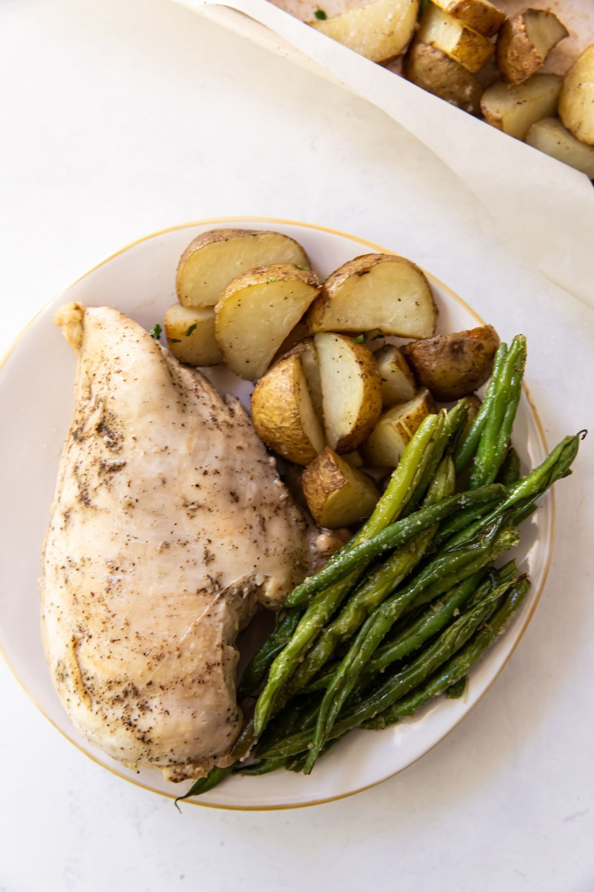 White plate with chicken breast, green beans, and potatoes