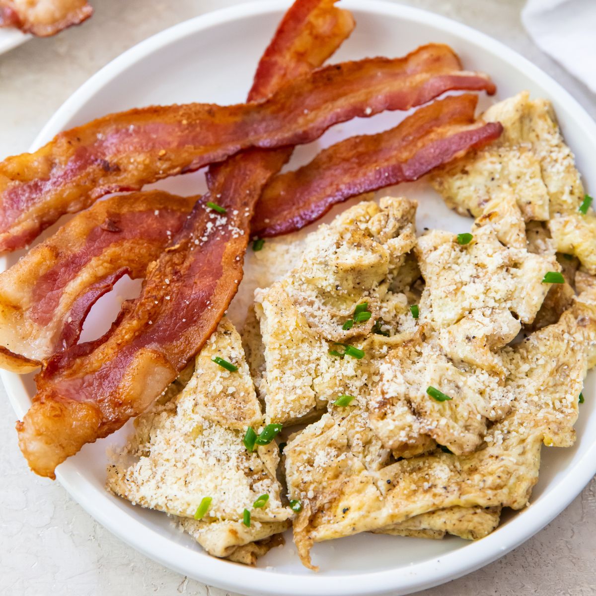 Blackstone scrambled eggs on a white plate with bacon