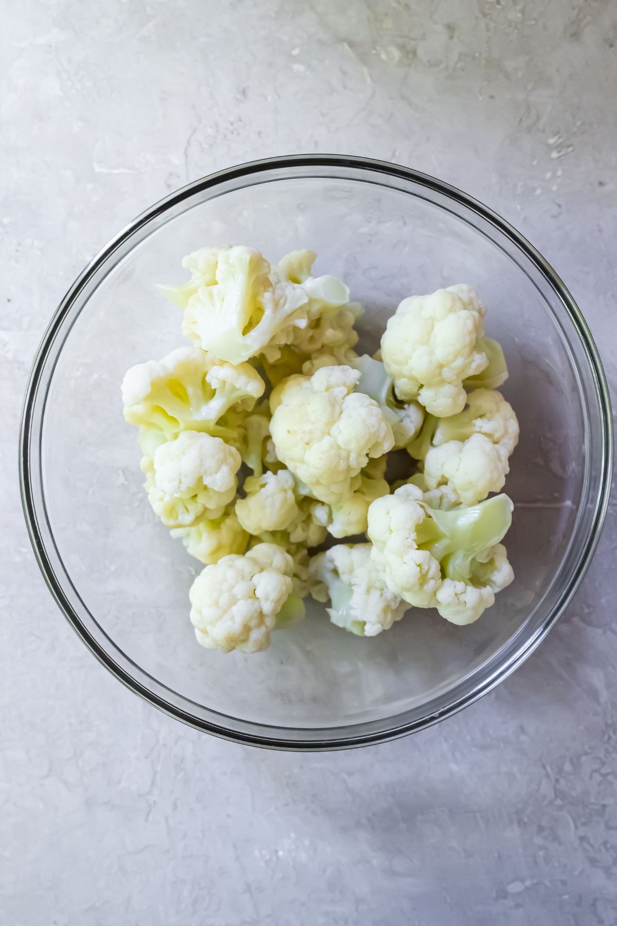 cauliflower sitting in a glass bowl on a white counter top.