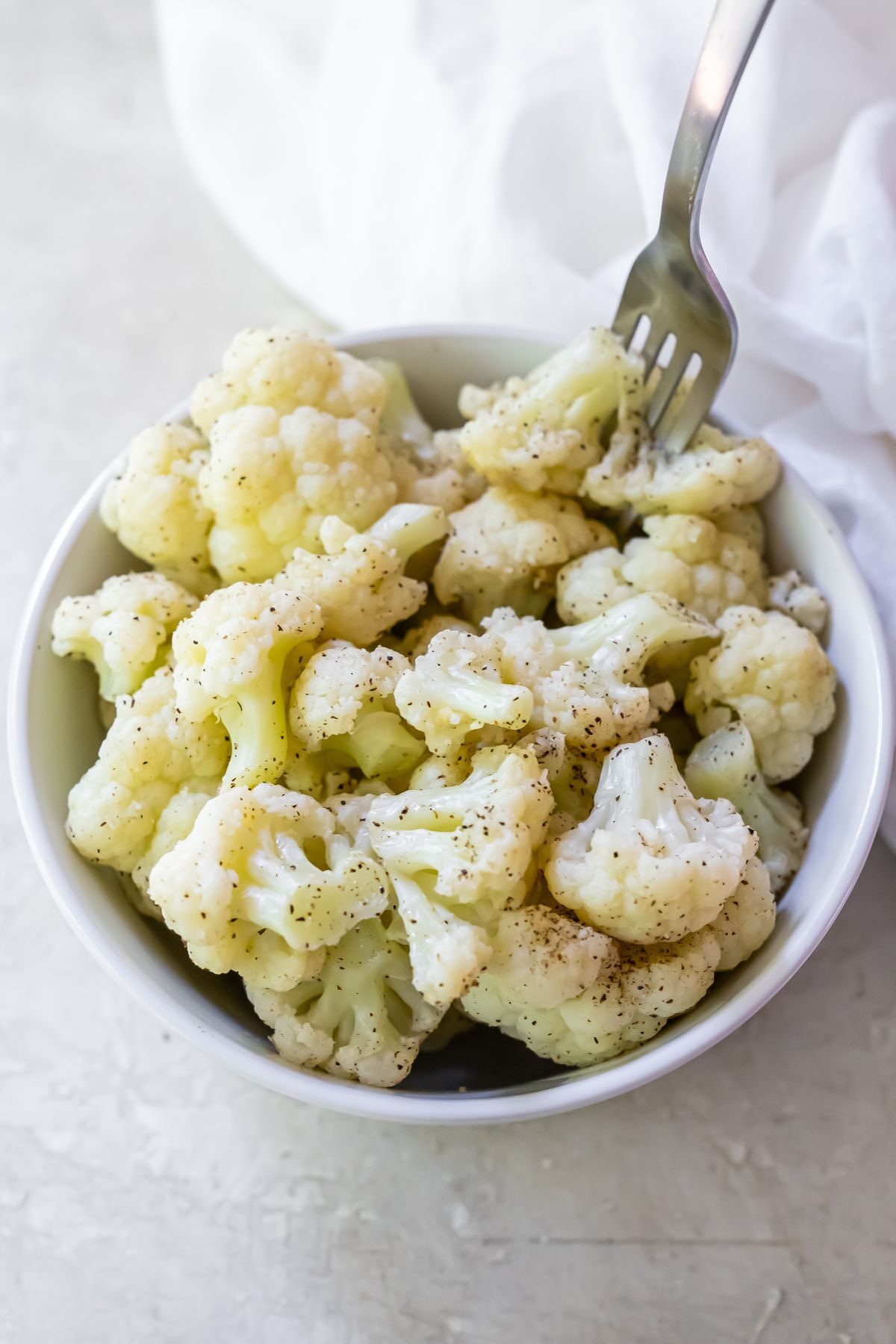 Cauliflower seasoned with salt and pepper sitting in a ceramic bowl on a white countertop