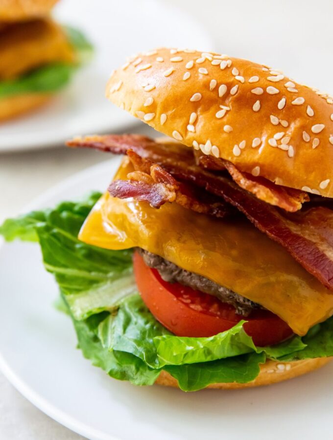 blackstone burger topped with cheese, bacon, lettuce, tomato on a white plate
