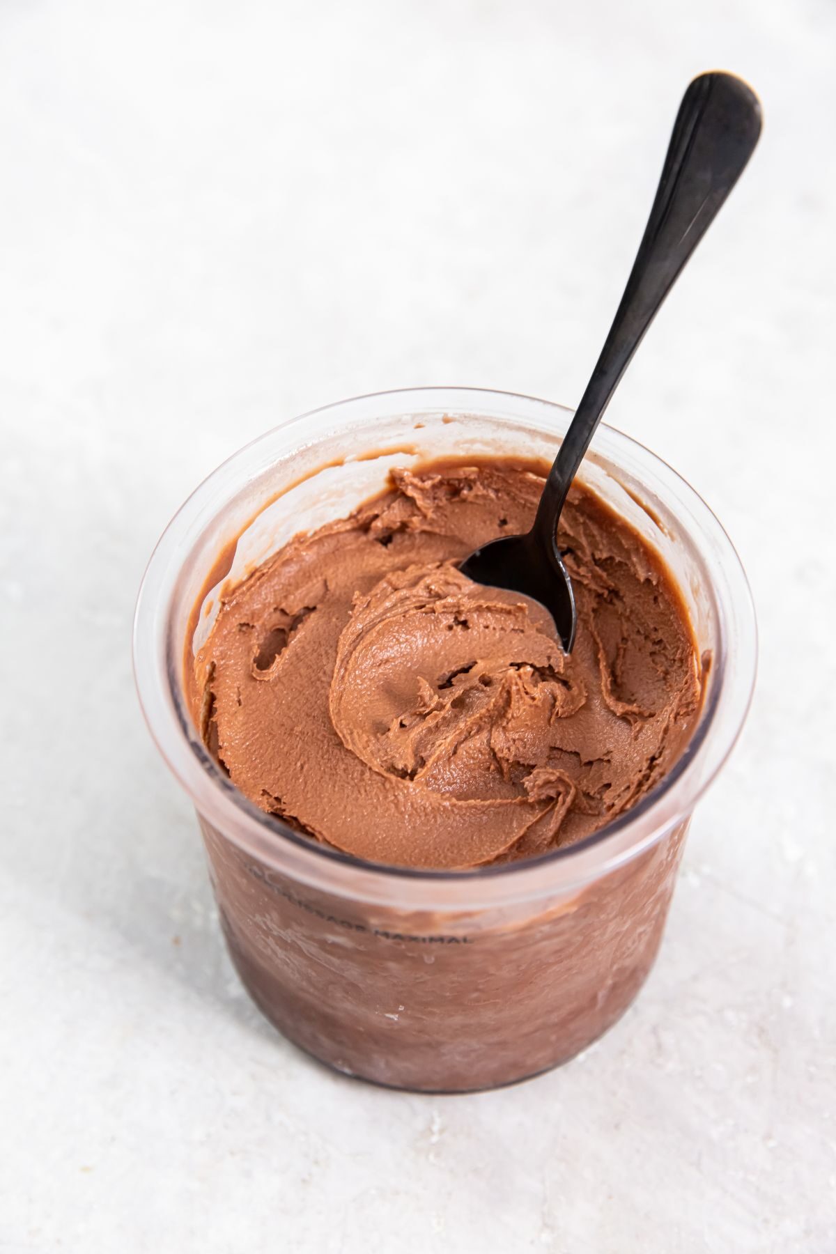 a pint of keto chocolate protein ice cream in a clear pint container with a spoon