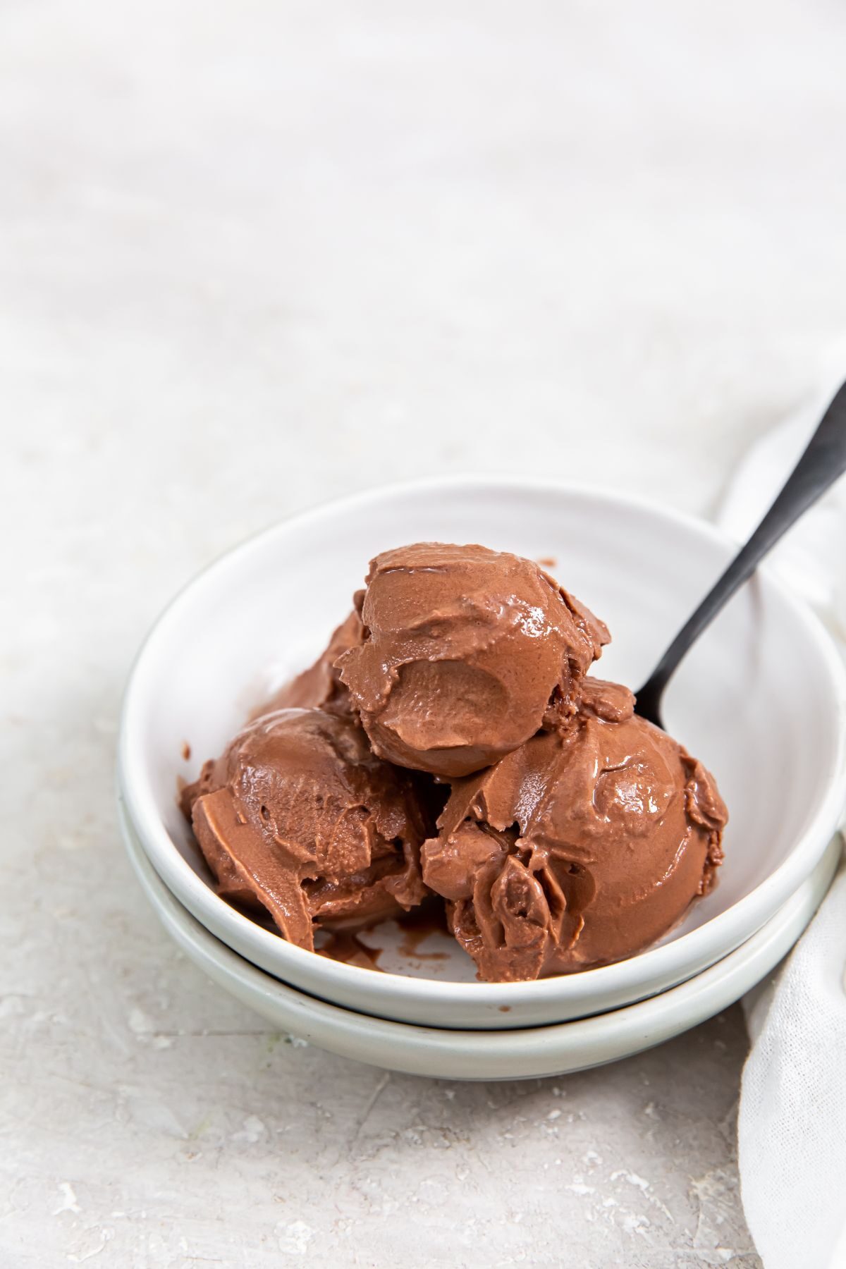 keto chocolate ice cream in a small bowl with a spoon wit a pint of ice cream