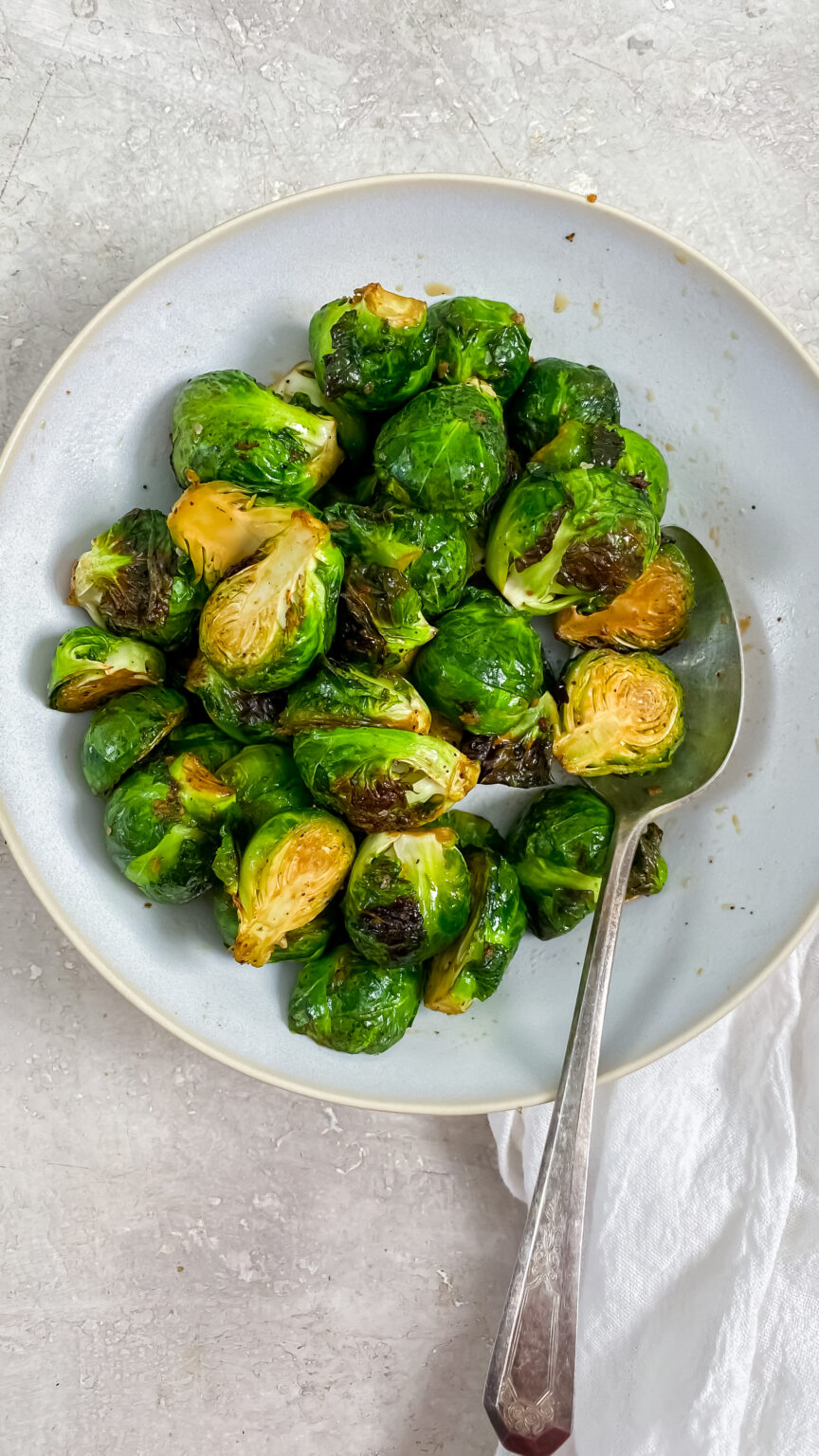 Air fryer Brussel Sprouts in a white bowl with a spoon.