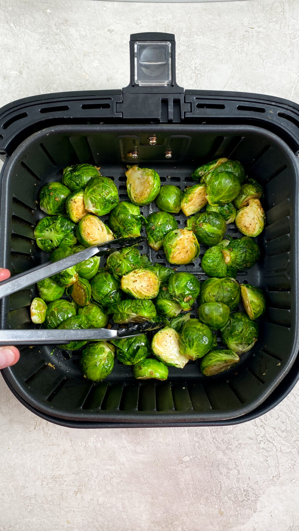 brussel sprouts being flipped in an air fryer basket