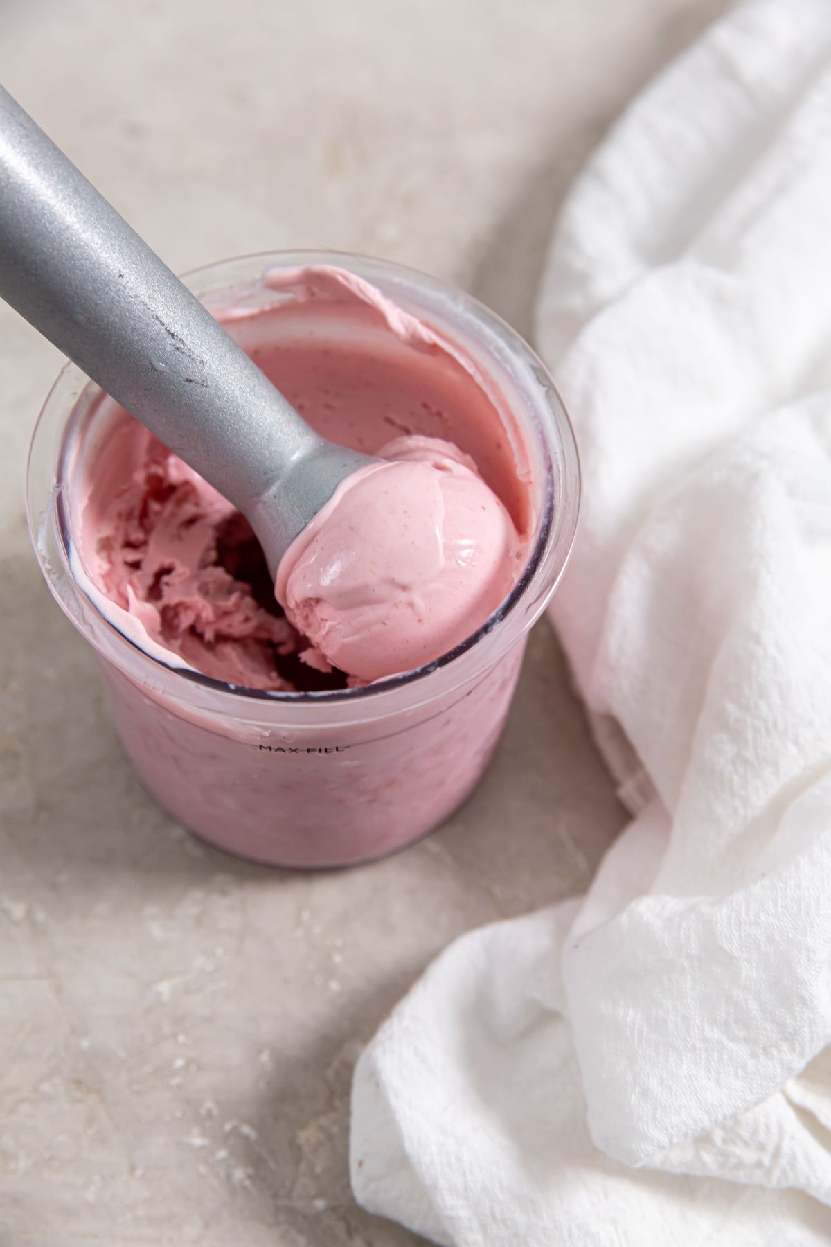 strawberry ice cream in a plastic pint container with an ice cream scoop