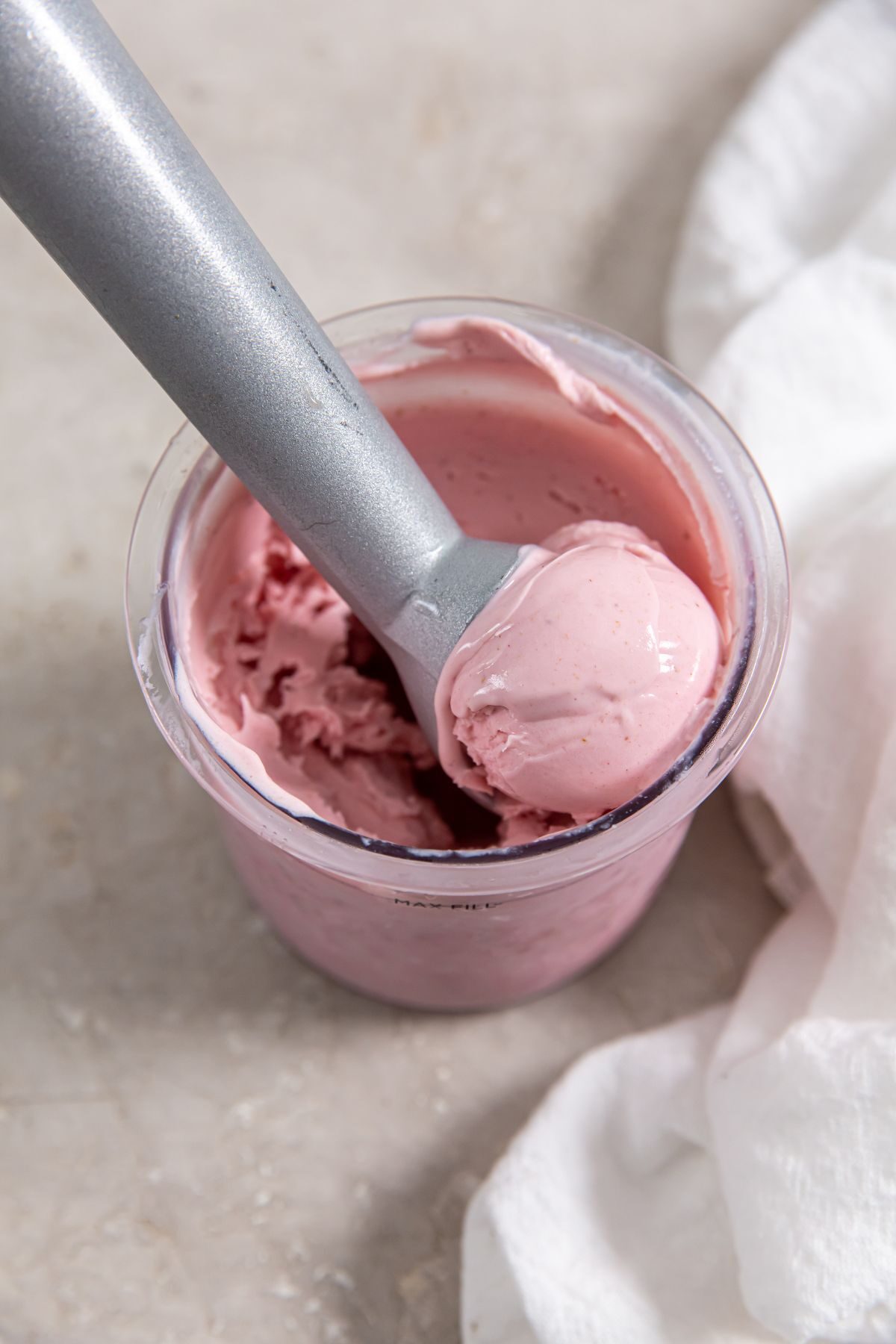 strawberry ice cream in a plastic pint container with an ice cream scoop