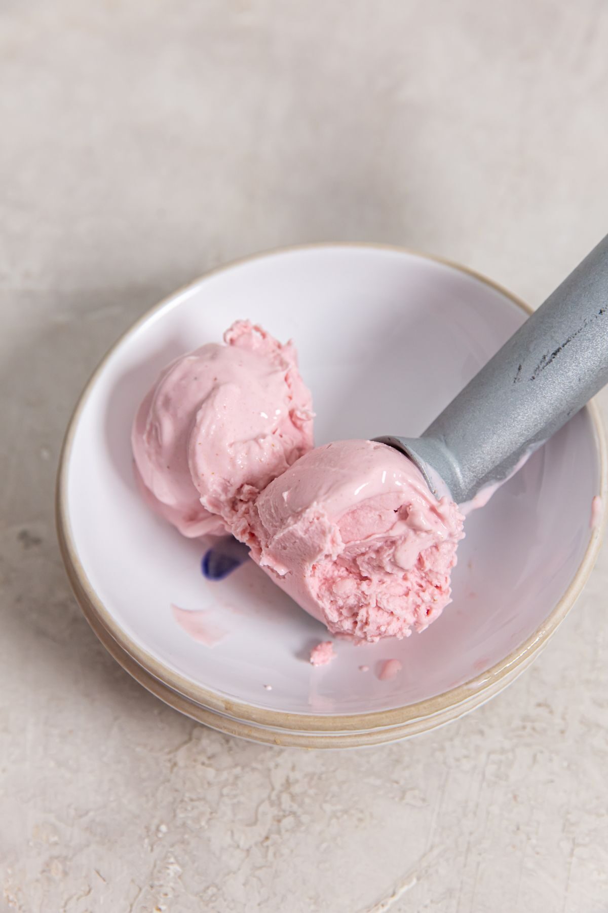Ninja Creami Strawberry ice cream in a small white bowl with an ice cream scoop