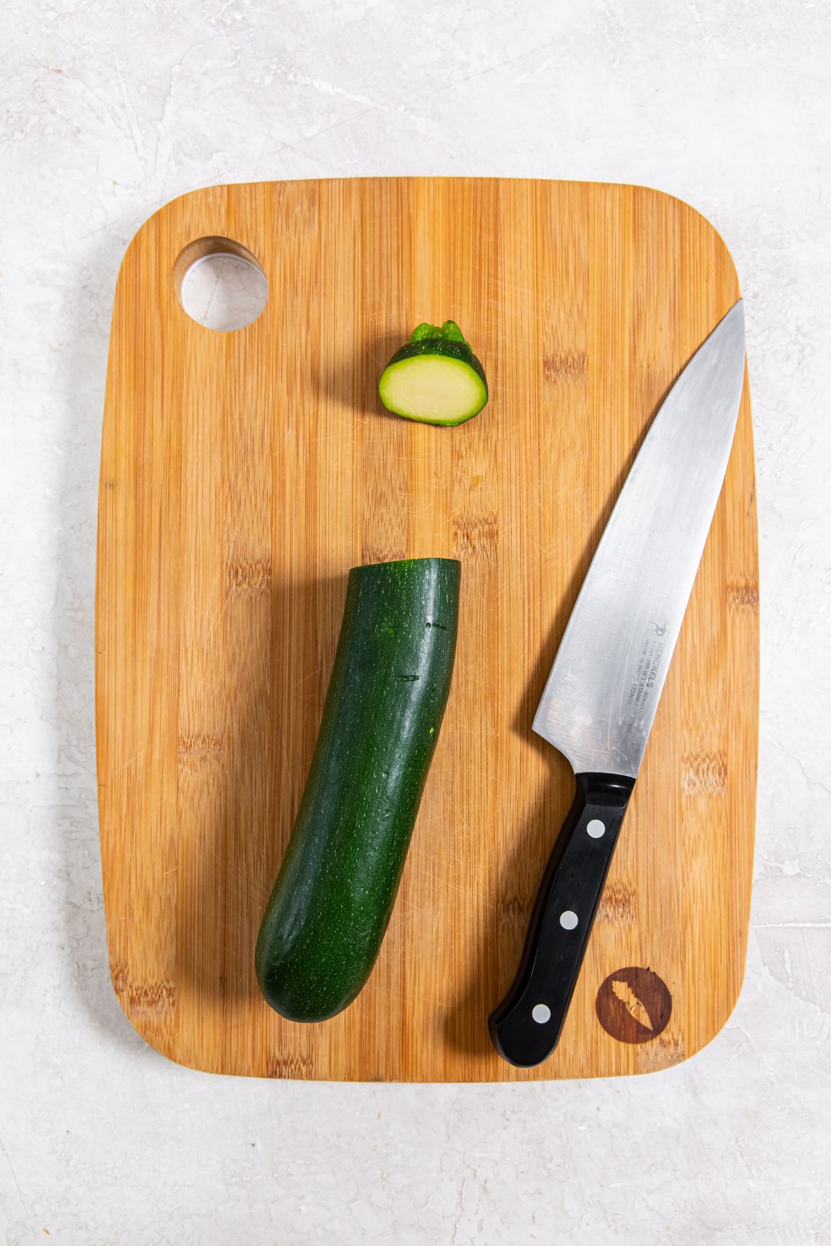 brown cutting board with zucchini and knife on top