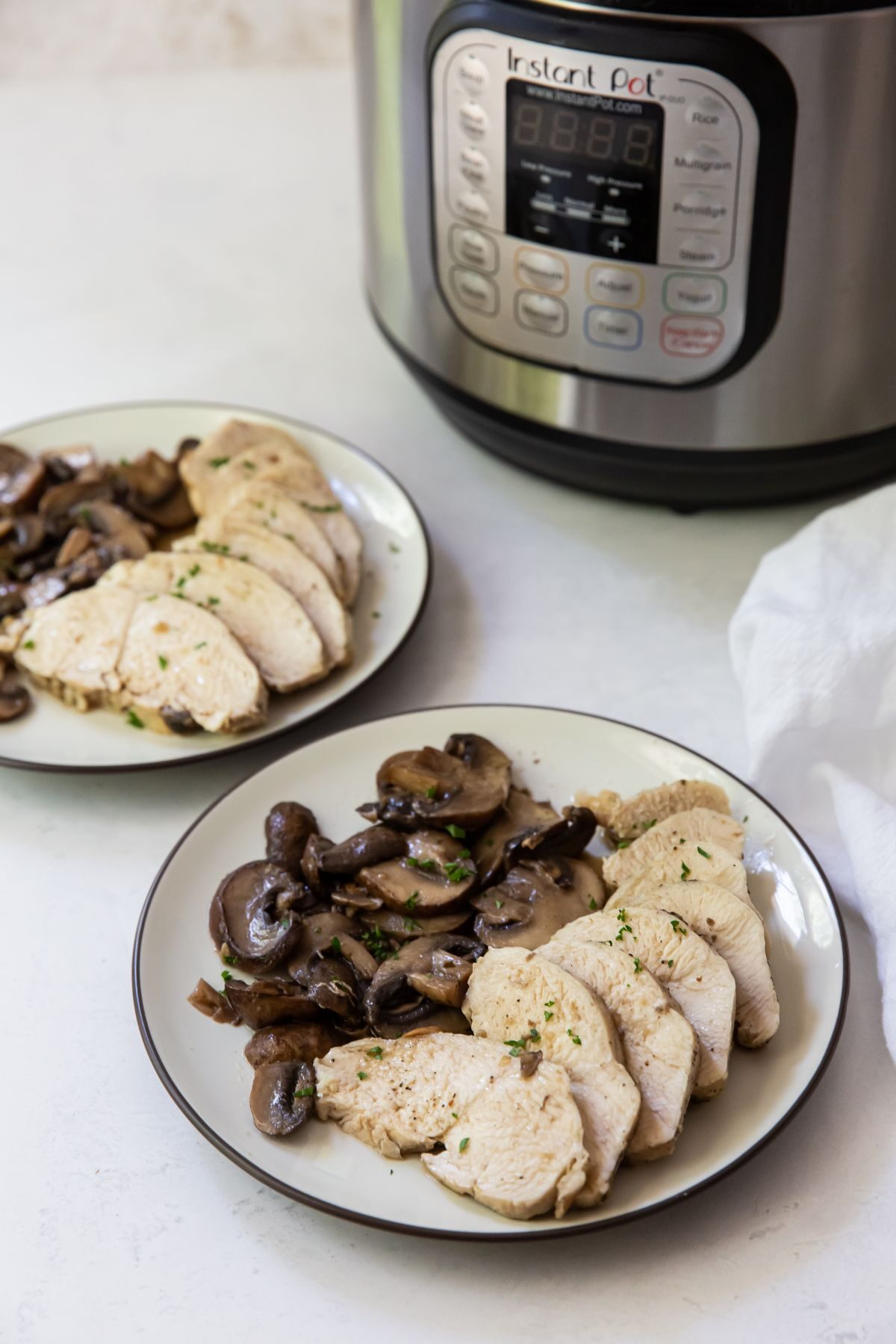 two plates of chicken breast and mushrooms with an instant pot in the background 