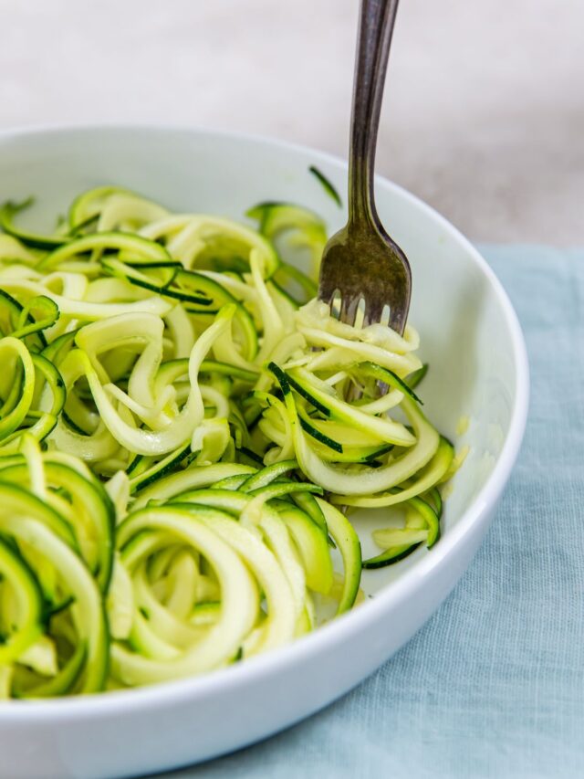 zoodles in a white bowl and fork inside bowl. blue towel next to it