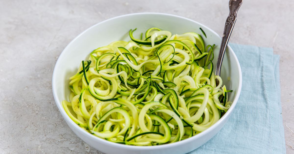 zoodles in a white bowl and fork inside bowl. blue towel next to it