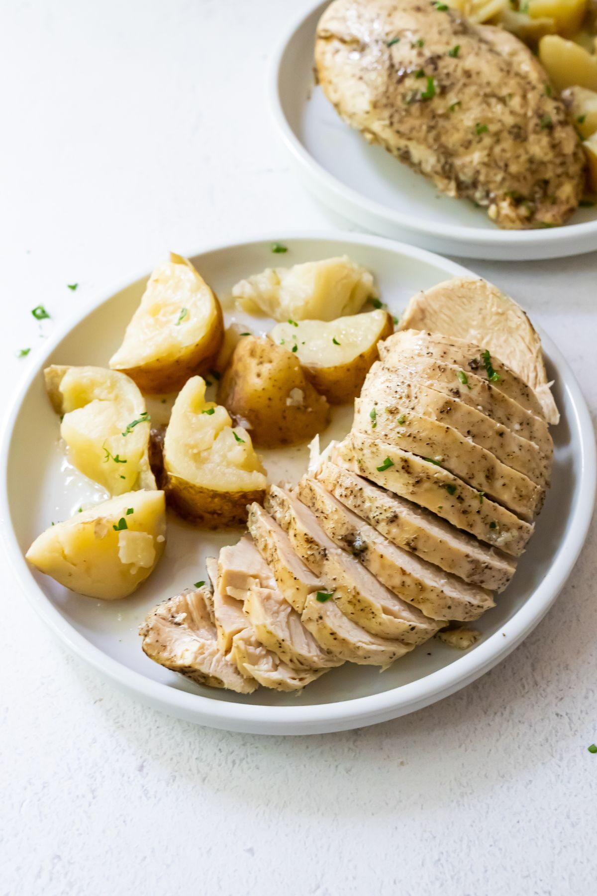 Cooked and sliced chicken with quartered potatoes on a white plate.