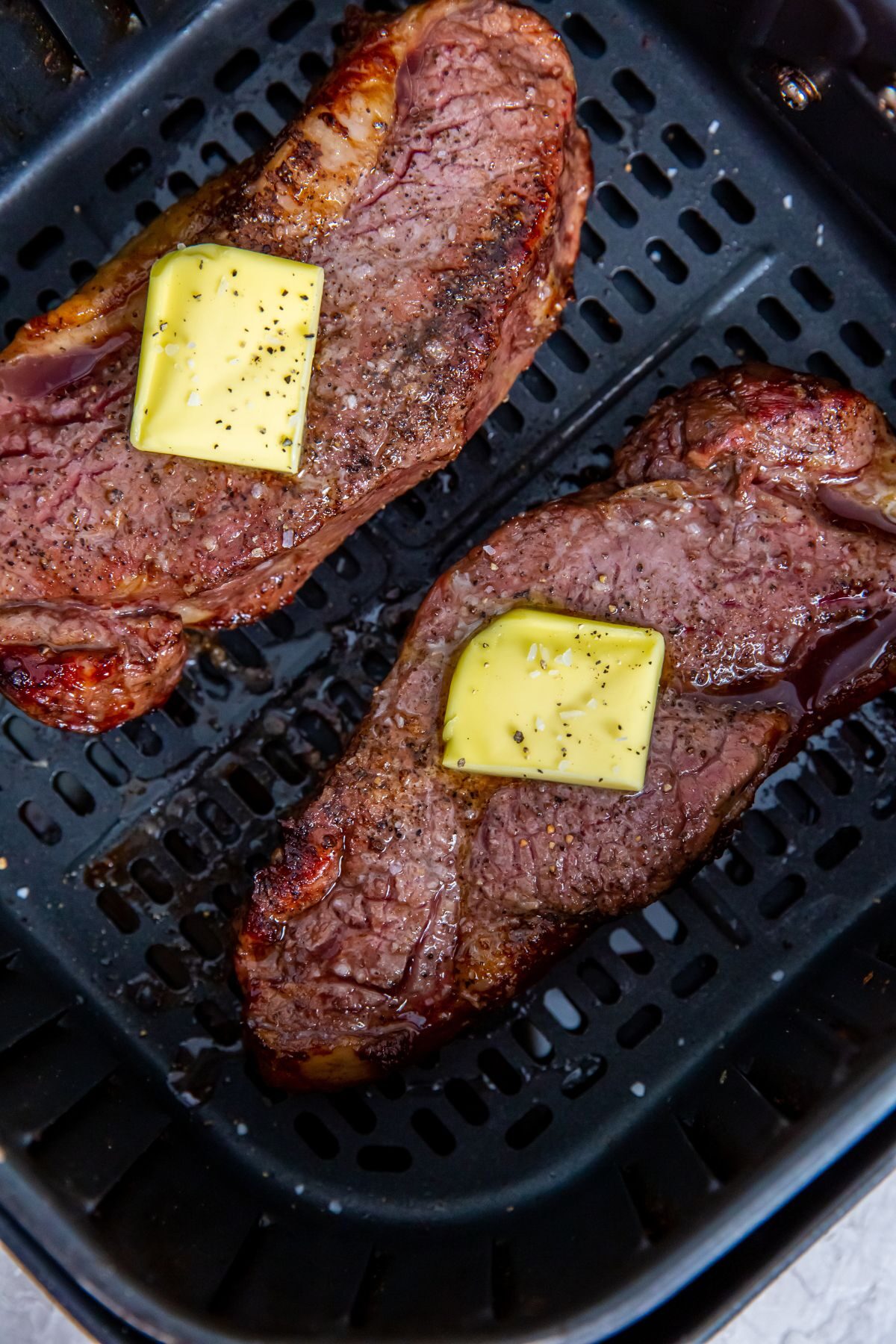 Cooked strip steaks in air fryer basket with tabs of butter on top