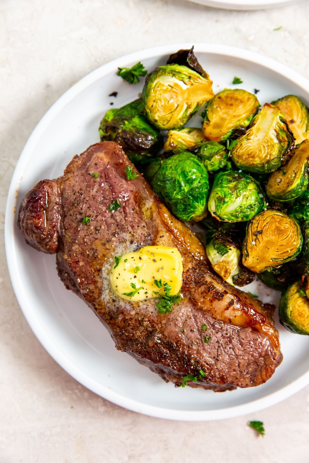 air fryer strip steak with tab of butter on top next to brussel sprouts on a white plate
