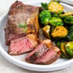sliced air fryer strip steak on white plate next to Brussel sprouts