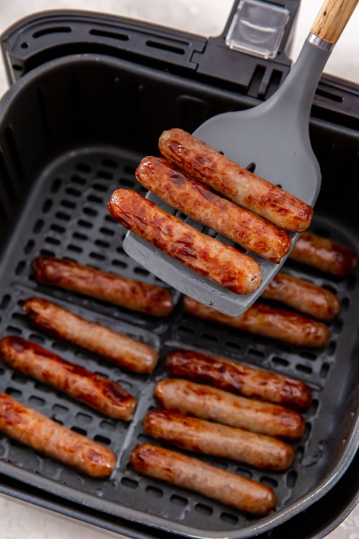 breakfast sausage in the air fryer basket with some on a spatula