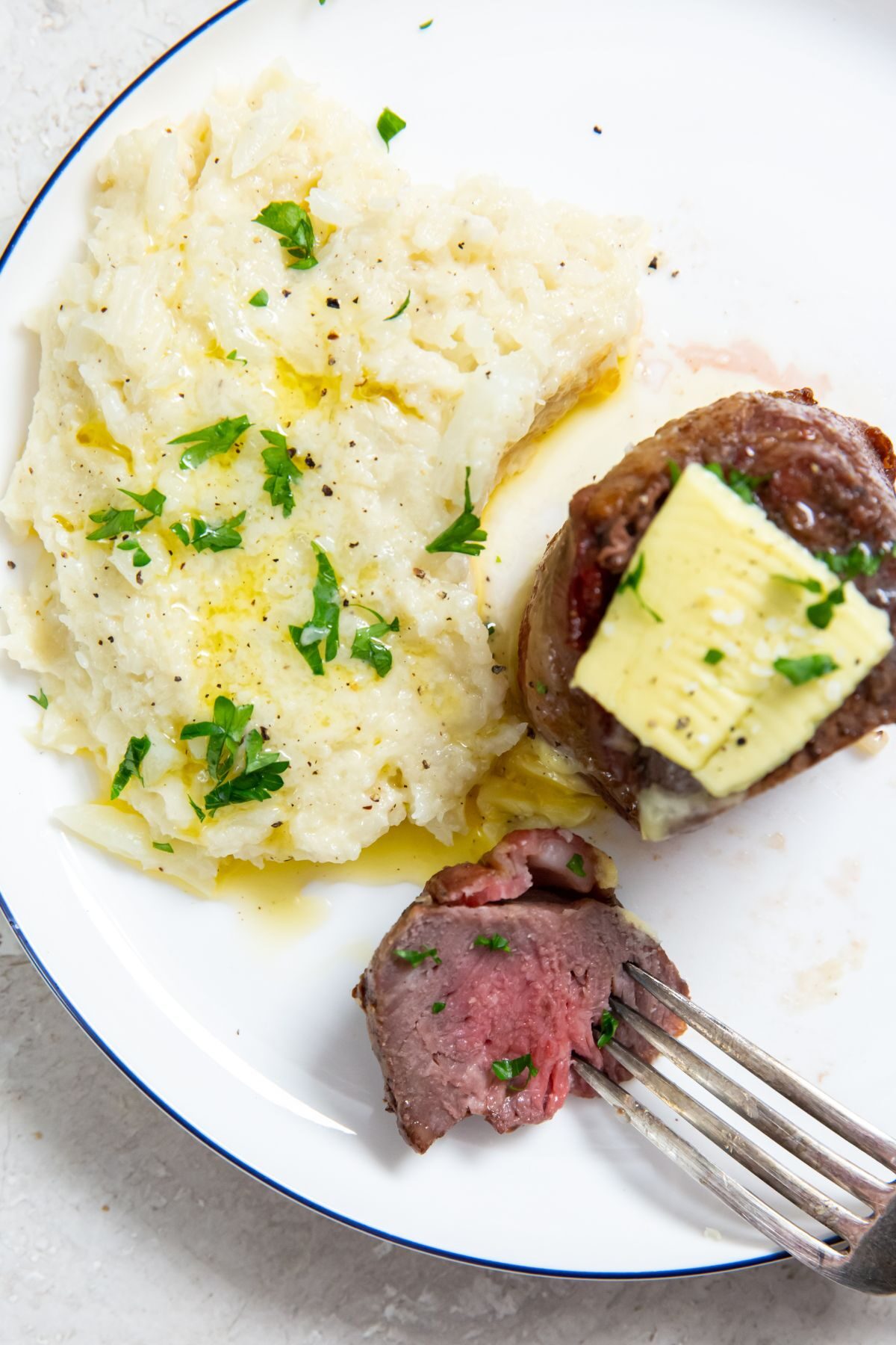 air fryer chuck filets with butter on top with cauliflower mashed on the side with a piece on a fork
