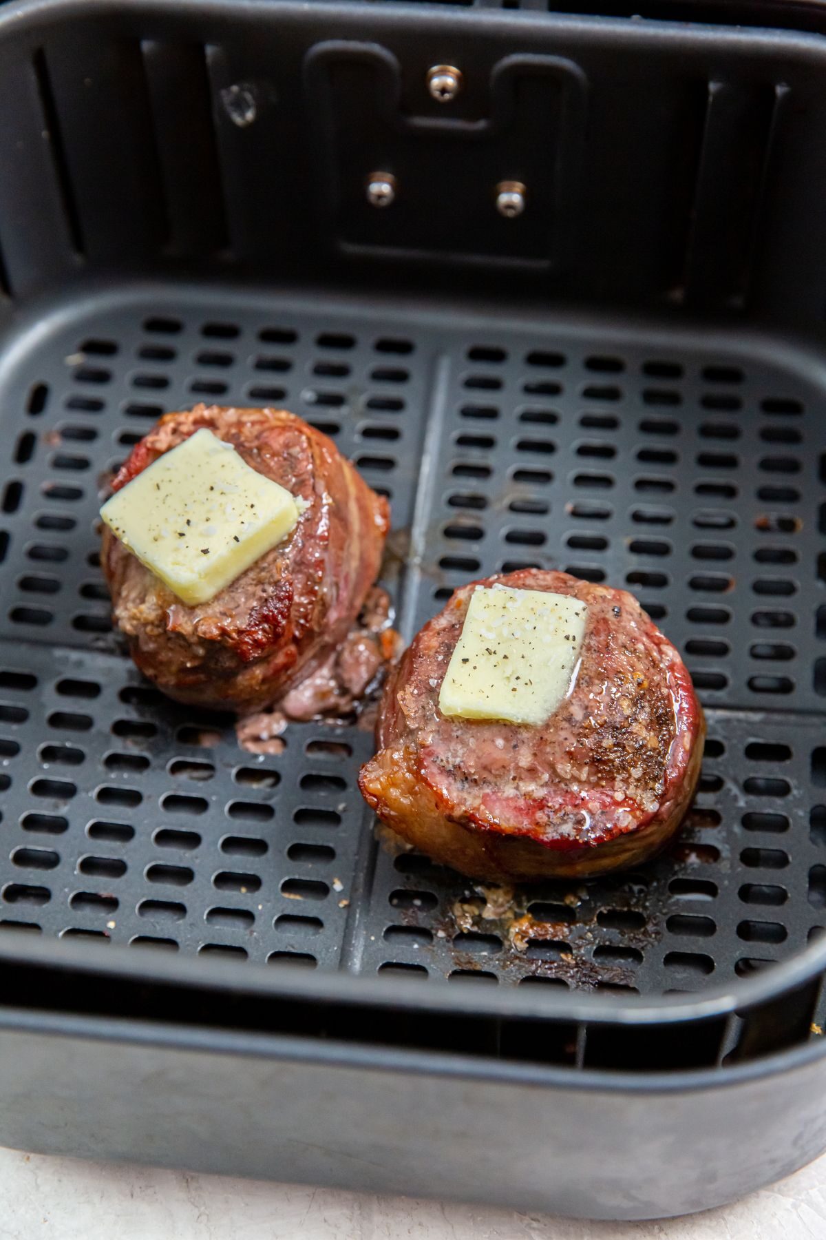 air fryer chuck filets with butter on top in the air fryer basket