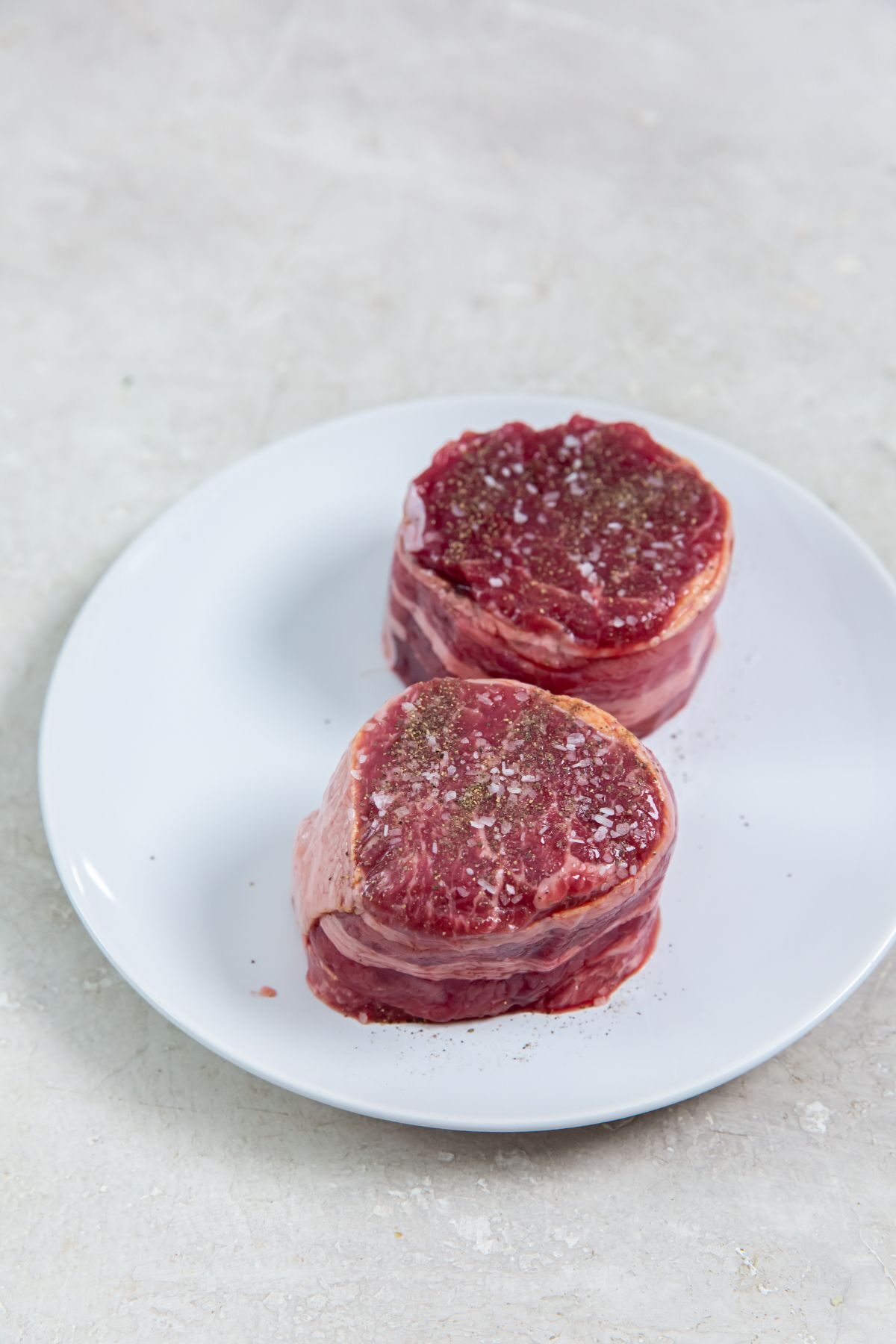 raw beef chuck on a white plate with salt and pepper.