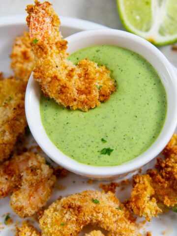 Air Fryer panko shrimp on a white plate dipped in green sauce
