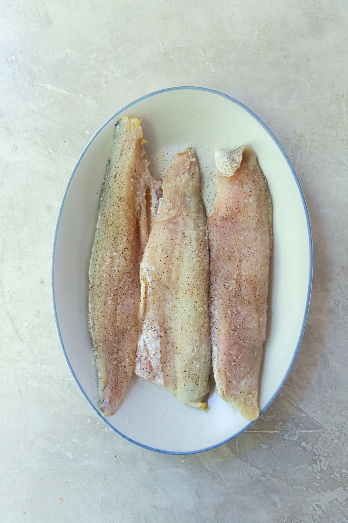 raw walleye with salt and pepper on a white dish