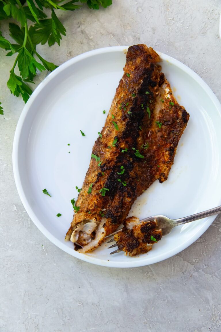 Blackened Walleye on a white plate with parsley and a fork.