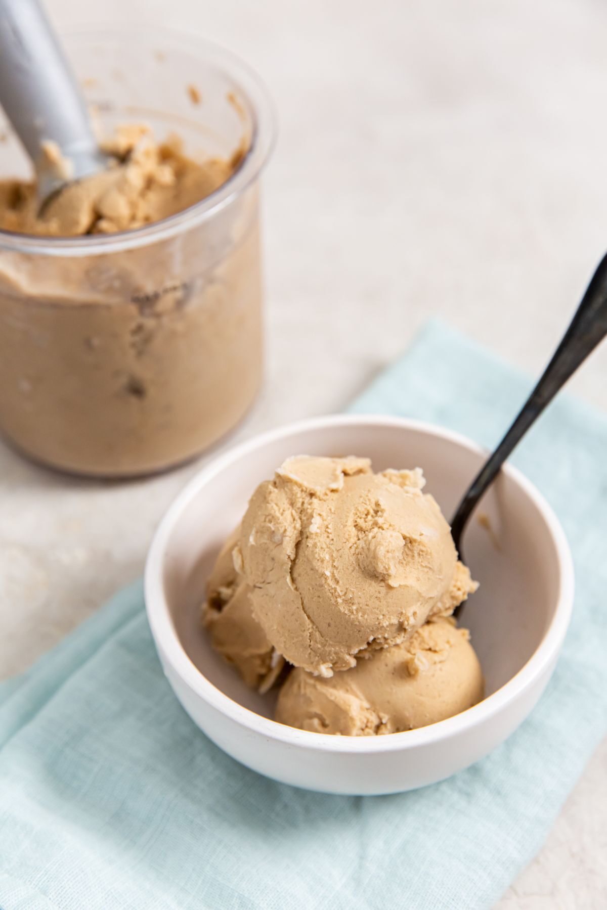 Coffee ice cream in a white bowl with a black spoon on a turquoise napkin