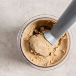 Coffee ice cream in a pint container with an ice cream scoop