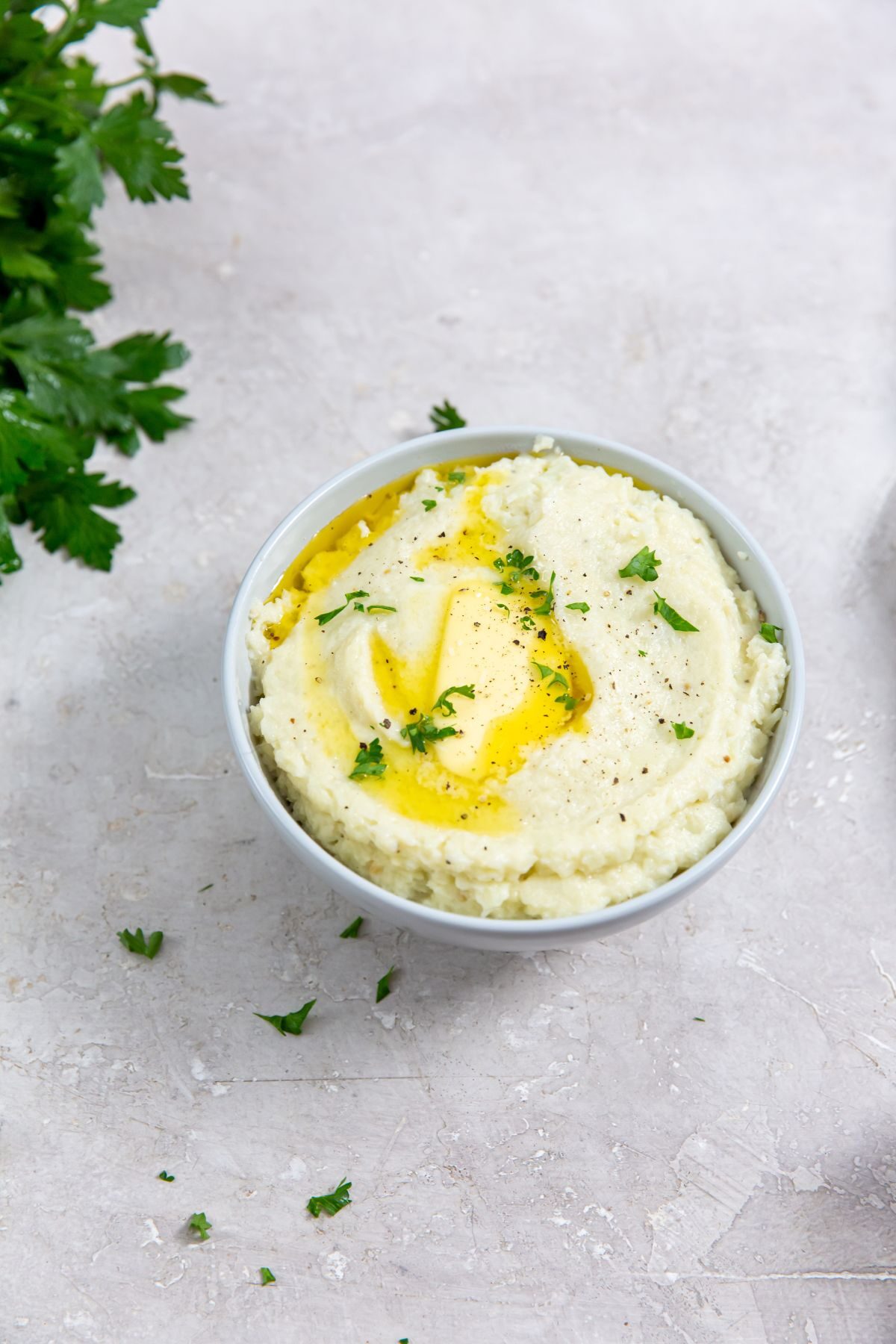 Instant Pot Cheesy Mashed Potatoes in a white bowl with parsley on the side.