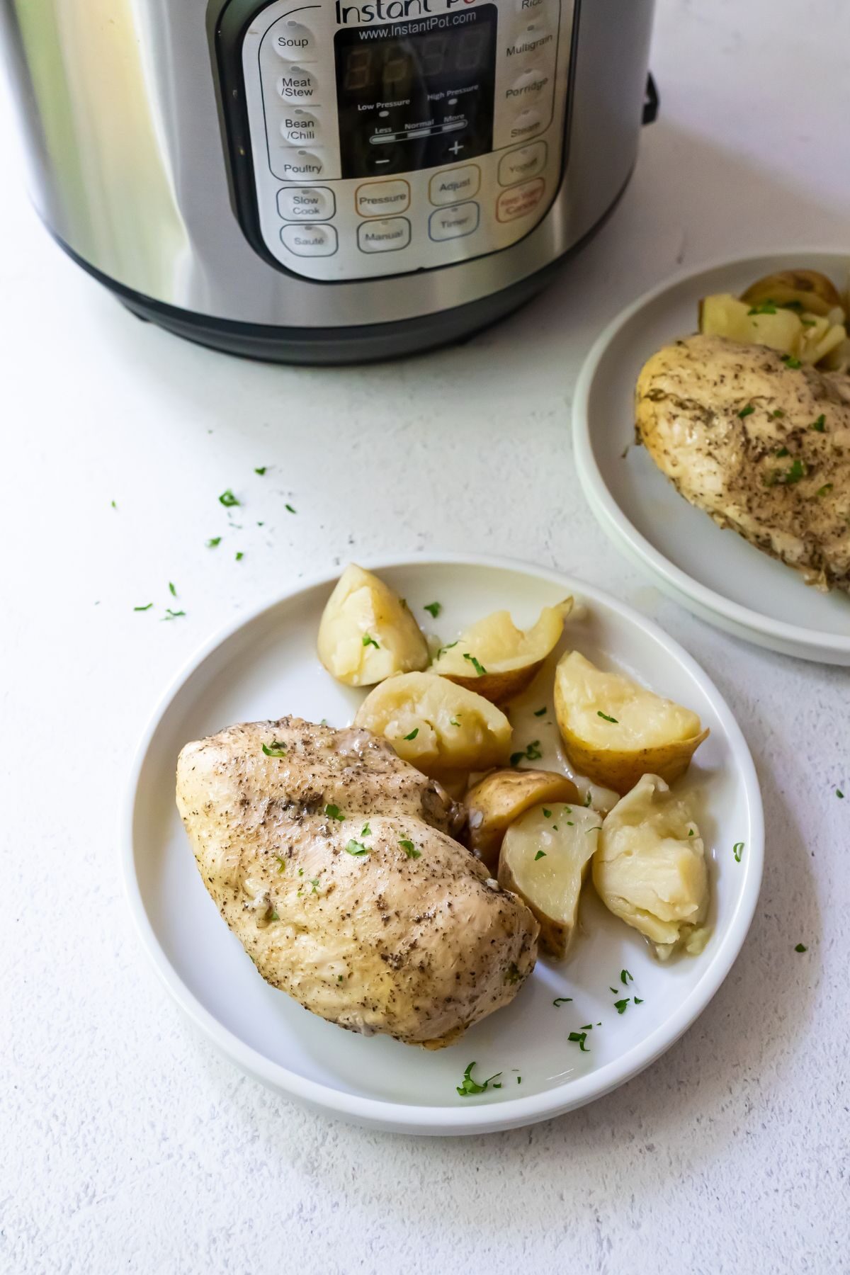 Cooked and seasoned chicken breast with quartered potatoes on a white plate with an instant pot in the background.