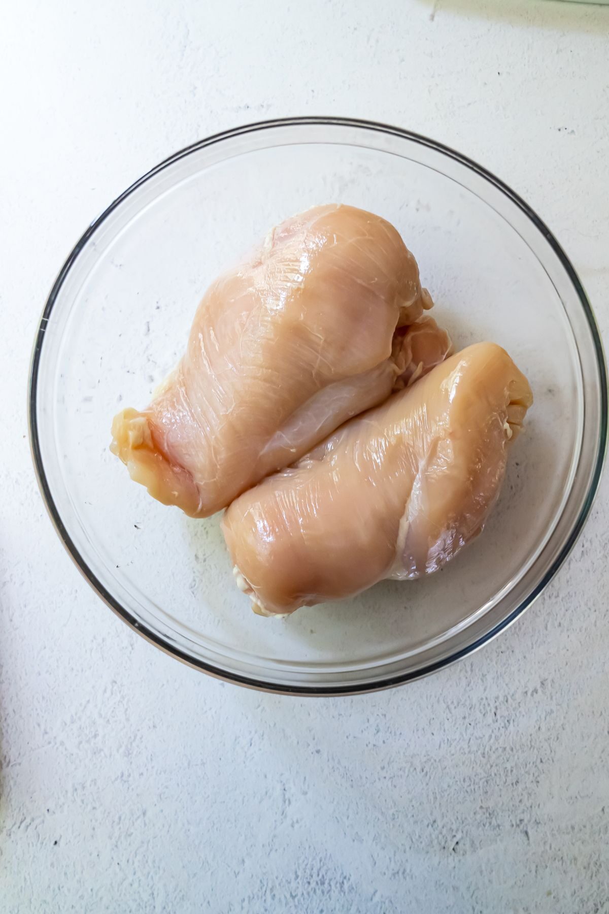 Two raw chicken breasts in a glass bowl.