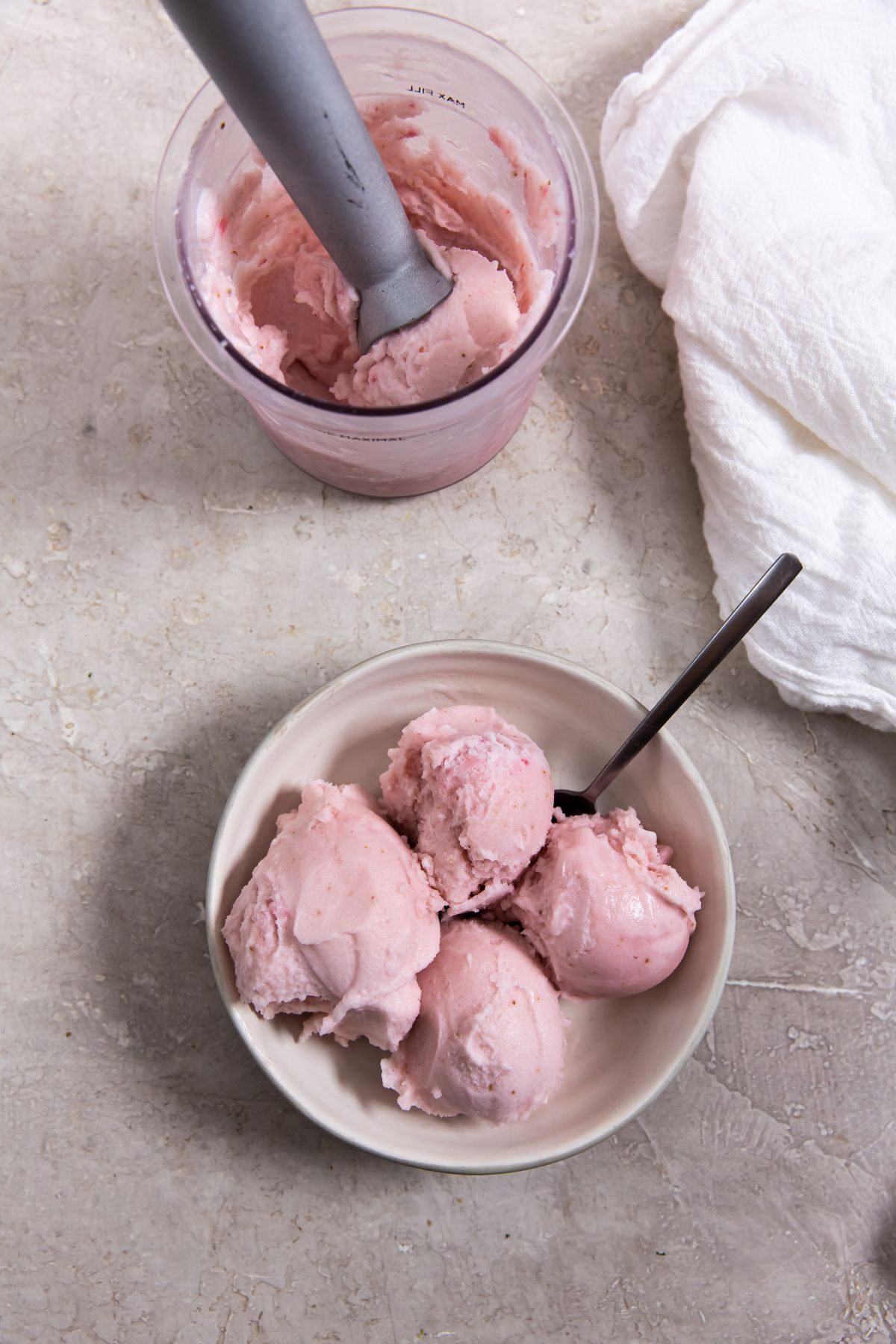 3 ingredient keto strawberry ice cream in a pint container with an ice cream scoop next to a bowl of ice cream with a spoon